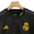 Camisa do Kit Infantil Real Madrid III 23/24 da Adidas, preta com detalhes em amarelo, destacando o logo do clube e a marca.