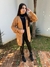 Mulher usando cardigan tricô marrom claro aberto, blusa preta de gola alta, calça preta e botas pretas em jardim com piso de tijolos