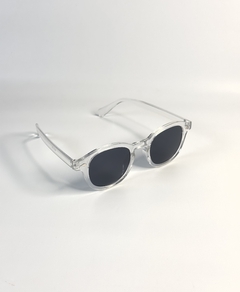 Gafas de sol con montura transparente y lentes oscuros, colocadas sobre una superficie blanca.