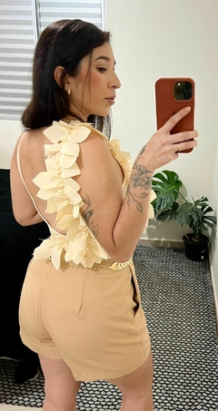 Body com flores na lateral subindo para alca e indo para as costas, decote em U, decote nas costas, alça finas, com um cinto de escamas e shorts na cor bege claro