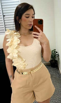 Body com flores na lateral subindo para alca e indo para as costas, decote em U, decote nas costas, alça finas, com um cinto de escamas e shorts na cor bege claro