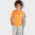 Camiseta infantil masculina laranja com estampa, usada por menino com cabelo cacheado.