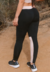 Calça legging fitness preta com detalhe em faixa chocolate, vista traseira, usada por uma modelo em ambiente outdoor.