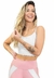 Modelo sorridente vestindo cropped fitness branco, com calça rosa, em fundo claro.