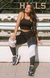 Modelo usando um conjunto fitness cropped preto com calça legging preta e faixas rosa e branco, posando ao ar livre.