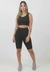 Conjunto fitness preto composto por bermuda e cropped, modelo feminino em pé, com tênis rosa em fundo neutro.