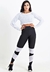 Mulher posando com um conjunto fitness, incluindo calça legging preta com detalhes brancos e cropped branco, em fundo neutro.