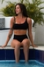 Biquíni preto top e calcinha cintura alta, modelo Le Paradis, com uma mulher sentada à beira da piscina.