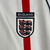 Camisa Retrô Inglaterra Home 2002 Umbro Branca com listra vertical vermelha, gola em V com ribana azul escura e escudo da seleção no peito. Modelo histórico da seleção inglesa, ideal para torcedores e colecionadores apaixonados por futebol e grandes conqu