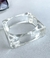 Bracelete de resina transparente com formato quadrado e espessura grossa, posicionado sobre uma superfície clara.