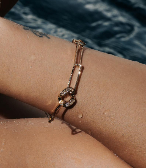 Pulseira elos semijoia banhada a ouro 18k com pingente cravejado de zircônias, adornando um pulso feminino.