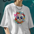 Camiseta oversized branca com estampa de caveira kawaii cercada por flores coloridas.