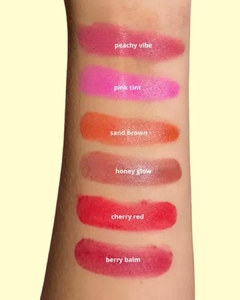 Amostra de blush cremoso em tons variados no braço, incluindo "peachy vibe", "pink tint", "sand brown", "honey glow", "cherry red" e "berry balm".