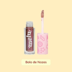 Gloss labial com brilho da marca Melu, na cor Bolo de Nozes, apresentado em um frasco transparente ao lado do aplicador com a ponta de espuminha e tampa rosa.