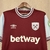 Camisa do West Ham United, temporada 2004/25, em fundo claro, com detalhes em azul e logo da Umbro.