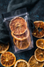Paquete de doypack con rodajas de pomelo deshidratado de la marca Botánicos del Paraná, rodeado de más rodajas de pomelo en una superficie oscura.