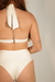 Mulher com cabelo ruivo usando top de biquíni branco com parte de trás amarrada e calça alta branca, exibindo tatuagens.