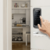 Mostra uma fechadura digital instalada em uma porta. O design moderno e o teclado touch são destacados. Ao fundo, é visível uma sala, sugerindo que o produto é ideal para ambientes residenciais ou comerciais.