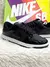 Tênis Nike SB Dunk Low Pro na cor preto com acabamento em verniz, apresentado sobre um fundo branco e uma caixa colorida da Nike.