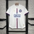 Camisa do Bahia 24/25 manto 1, branca com detalhes em azul e vermelho, pendurada em um suporte.