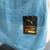 Detalhe do selo de autenticidade da camisa versão jogador do Manchester City, coleção 24/25, com logo da Puma em fundo azul.
