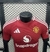 Camisa versão jogador do Manchester United, cor vermelha, com logo da equipe e detalhes em branco.