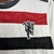 Detalhe da camisa do Manchester United, temporada 24/25, com listras vermelhas e pretas e logo do clube.