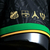 Detalhe da camisa preta The Prince Neymar Jr 10 da Comma Football, com escudos de clubes em dourado e detalhes em verde e amarelo.