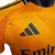 Detalhe da camisa versão player do Real Madrid 2024/2025, em tom laranja com logo da Adidas e nome do patrocinador.