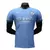 Camisa versão jogador do Manchester City, na cor azul, com logo da equipe e detalhes em preto nas mangas.