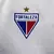 Emblema da camisa do Fortaleza 24/25, apresentando o escudo em destaque com as cores azul, vermelho e branco, acompanhado de uma estrela dourada.