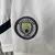 Emblema do Manchester City em um kit infantil da temporada 2024/25, em fundo branco.
