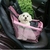 Cadeirinha de carro para pets com um cachorro branco dentro, em um assento de carro, com proteção em malha e cor rosa.