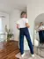 Modelo usando jeans azul para embarazadas, de espaldas, con blusa blanca en un ambiente interior moderno.