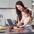 Uma mãe e sua filha cortando legumes na cozinha, com um suporte para celular e tablet em destaque na mesa.