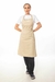 Modelo usando un delantal de cocina beige sobre una camiseta blanca y pantalones a rayas.