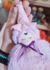 Chaveiro de bruxinha lilás com cabelo cacheado, vestido de tule e chapéu rosa, segurado por uma mão.