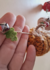Uma mão segurando um cordão decorativo com abóboras de crochê e um detalhe em forma de folha verde.
