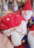 Gnominho Mágico com um chapéu vermelho de feltro e detalhes brancos, segurando um pequeno objeto, em meio a outros gnomos artesanais.