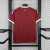 Camisa vermelha da seleção do Catar para torcedor, modelo masculino, com detalhes brancos nas mangas e gola, logo da Adidas e emblema da Federação de Futebol do Catar
