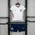 Kit infantil da seleção da Inglaterra para a Copa 2026, com camisa branca e detalhes em vermelho e preto, e shorts azul escuro com logo Nike e escudo da seleção
