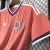 Camisa masculina rosa da seleção da Escócia para a Copa 2026, com listras verticais finas em azul, gola em V azul com detalhes brancos e logo Adidas branca no peito