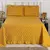 Kit Colcha Casal na cor laranja mostarda, da linha Bella da Sulamita Enxovais. O conjunto inclui a colcha com detalhes matelassê em losangos e babado na borda, e duas capas de travesseiro com bordado de folhagens em marrom e babados. A foto mostra o conju