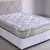 Pillow Top Casal Suavitec branco acolchoado sobre um colchão de casal com detalhes em bege e branco. O pillow top é preso ao colchão por elásticos laterais em cada canto. A cama possui uma base box branca texturizada e uma cabeceira estofada clara com cos