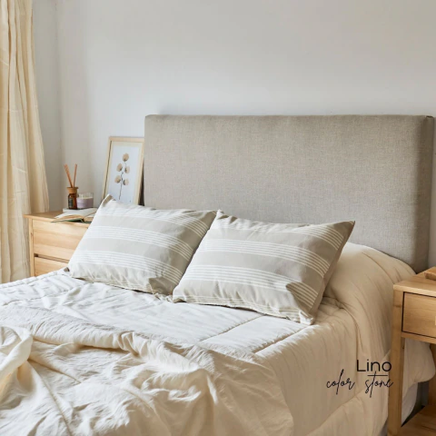 ​Respaldo de cama tapizado liso en lino color stone, ambientado con mesas de luz de madera natural de álamo y ropa de cama a tono.