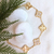 Pulseira em ouro 18K com detalhes em zircônias, inspirada em Virginia Fonseca, sobre um fundo claro com pedras brancas e folhas verdes.