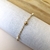 Pulseira em ouro 18K com quatro bolinhas e pérolas, disposta sobre um fundo claro.