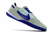 Chuteira Nike Streetgato Futsal cinza claro com detalhes em roxo e sola texturizada.