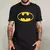 Camiseta preta unissex com estampa amarela do símbolo do Batman, usada por um homem tatuado.