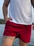 Homem usando short vermelho liso, posando à beira de um lago com camiseta branca.